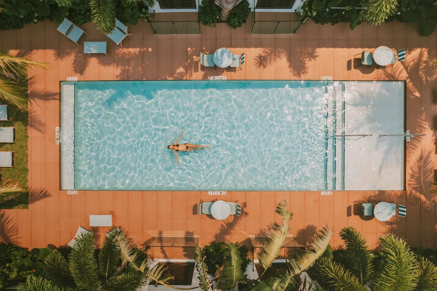 Aerial view of the courtyard pool with a guest swimming, teak deck at its edge.