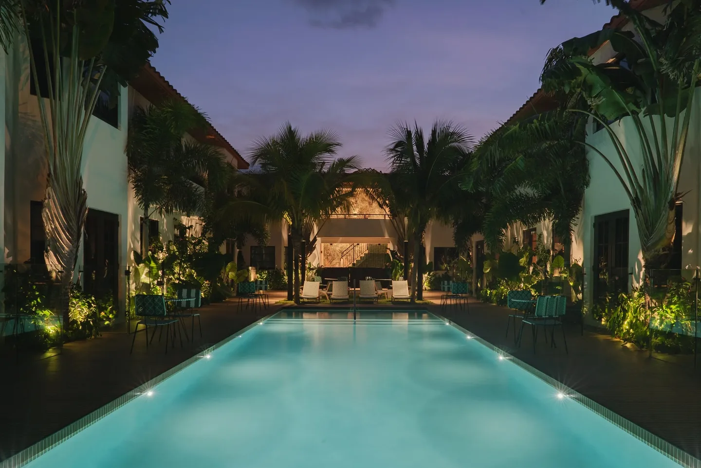 The courtyard pool at night, lit warm, palms and chairs around it.