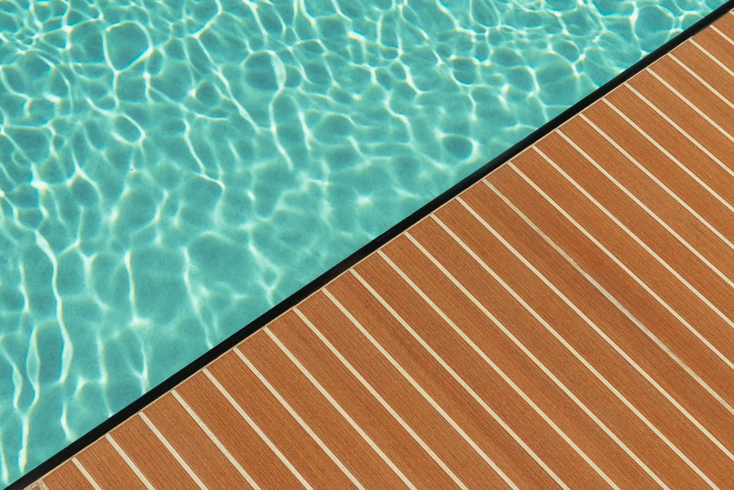 Close detail of the striped teak decking beside the pool water.