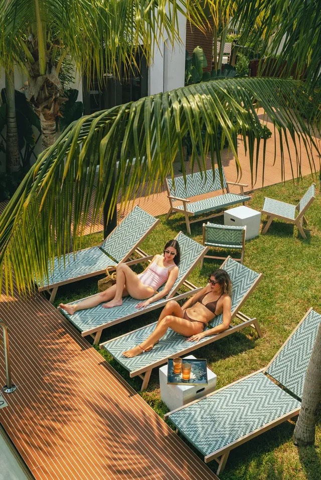 Two guests on loungers under a palm beside the courtyard pool.