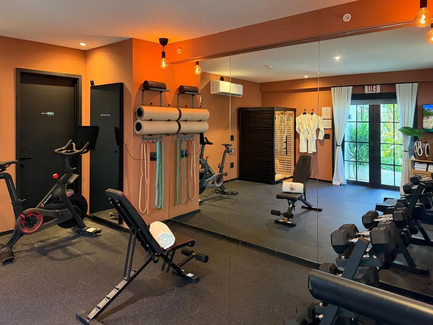 Gym with exercise bikes, an adjustable bench, dumbbells, yoga mats and resistance bands before a full mirror wall